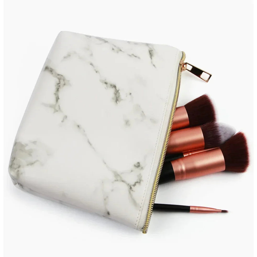 Astuccio trucco effetto marmo con cerniera dorata, contenente pennelli make-up professionali. Accessorio cosmetico elegante e funzionale.