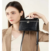 Donna con borsa a tracolla nera effetto coccodrillo, chiusura con zip, manico superiore. Elegante accessorio moda femminile.