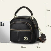 Borsa a tracolla nera in pelle PU con logo "K", tasca frontale con zip, dimensioni 22x13x19 cm, accanto a uno smartphone per confronto.