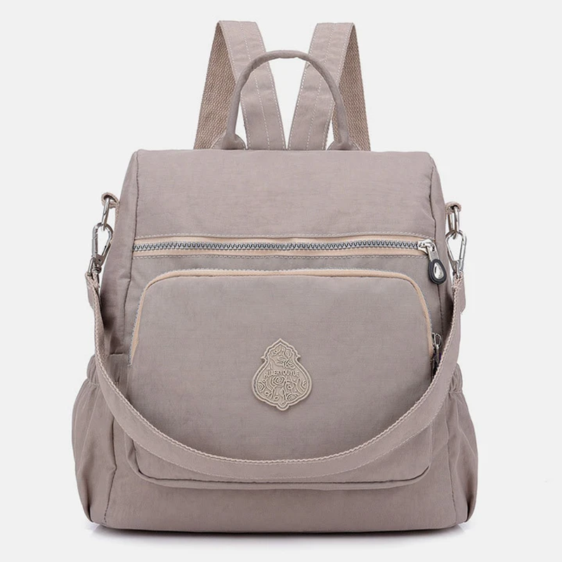 Zaino beige in tessuto impermeabile con tasca frontale con zip, spallacci regolabili e manico superiore. Design elegante e pratico per uso quotidiano.