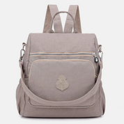 Zaino beige in tessuto impermeabile con tasca frontale con zip, spallacci regolabili e manico superiore. Design elegante e pratico per uso quotidiano.