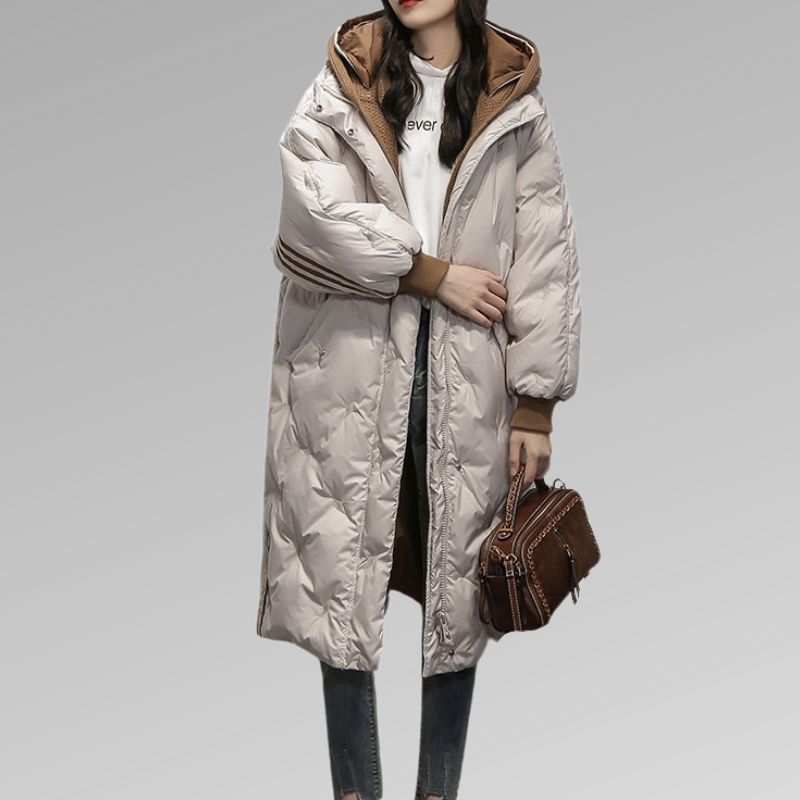 Giacca invernale lunga da donna, imbottita, colore bianco, con cappuccio marrone, abbinata a jeans e borsa marrone. Moda casual invernale.