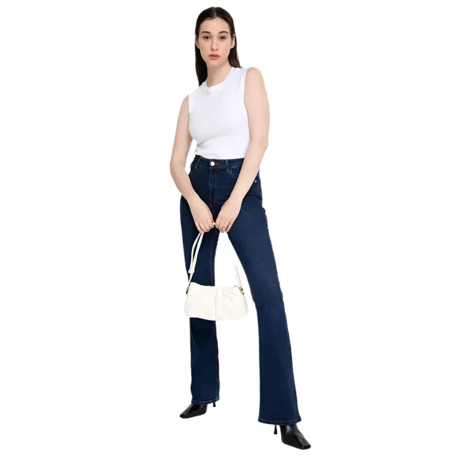 Donna in jeans a zampa blu e top bianco, con borsa bianca e stivali neri. Moda casual femminile, abbigliamento trendy, stile moderno.