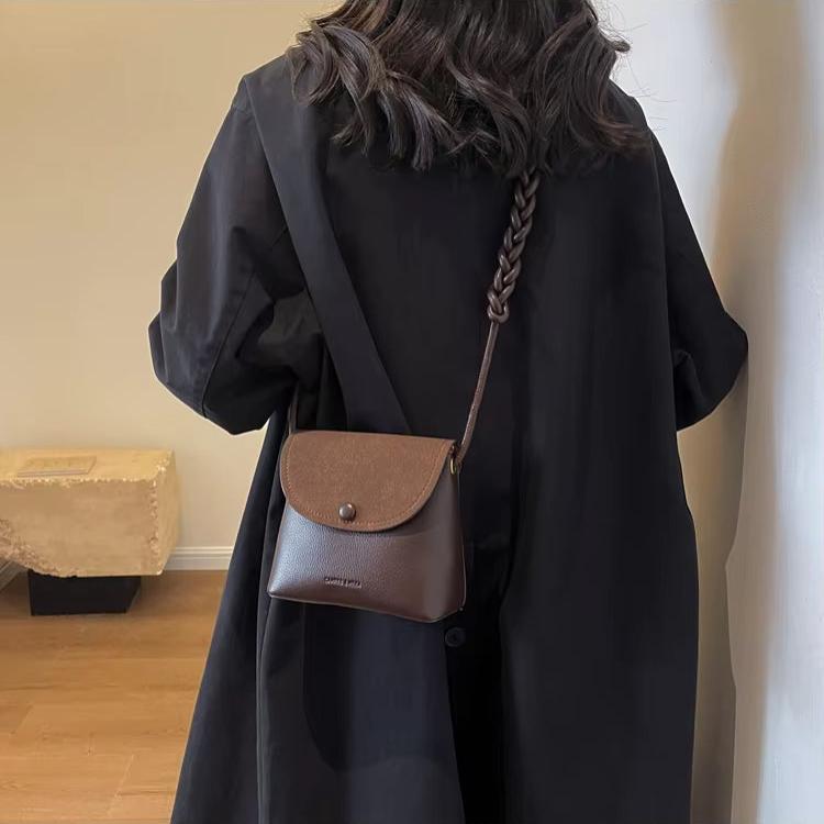 Donna con cappotto nero e borsa a tracolla marrone in pelle, design elegante e minimalista, moda autunno, accessorio femminile di tendenza.