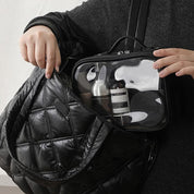 Borsa nera trapuntata con tasca trasparente contenente prodotti cosmetici, ideale per viaggi e organizzazione, moda e praticità.
