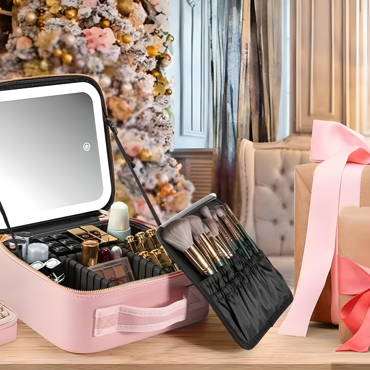 Astuccio trucco rosa con specchio LED, pennelli e cosmetici, davanti a un albero di Natale decorato e un regalo incartato con nastro rosa.