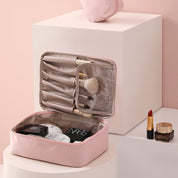 Astuccio da trucco rosa aperto con pennelli, cosmetici e rossetto rosso su sfondo rosa. Organizzatore make-up elegante e funzionale.