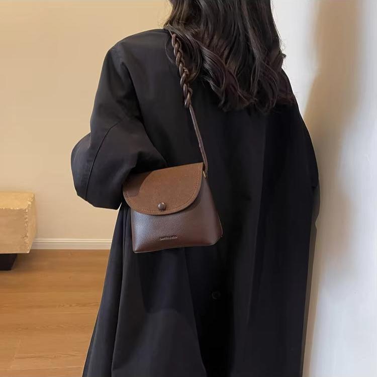Donna con cappotto nero e borsa a tracolla marrone in pelle, design minimalista. Accessorio moda elegante, perfetto per look autunnali.