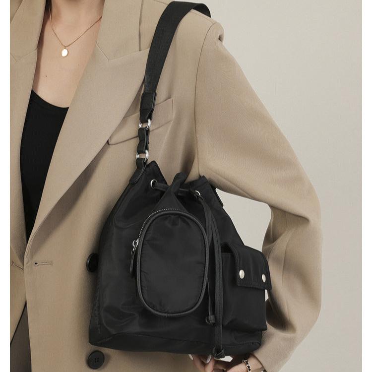 Borsa a tracolla nera in nylon con tasche multiple, indossata su cappotto beige. Design elegante e funzionale, ideale per moda urbana.