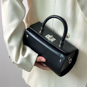 Elegante borsa a mano nera in pelle, design moderno, chiusura metallica, indossata con giacca bianca. Accessorio moda donna di lusso.