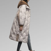 Giacca invernale donna lunga, imbottita, colore grigio chiaro, con cappuccio marrone, dettagli a righe, ideale per moda autunno-inverno.
