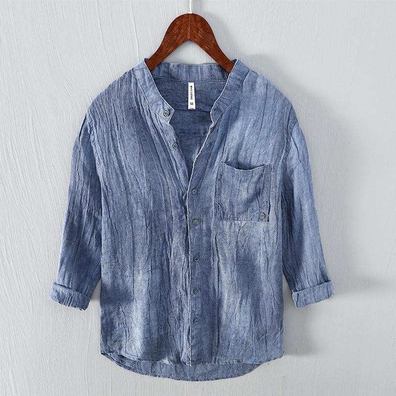 Camicia di lino blu da uomo, maniche lunghe, colletto alla coreana, tasca frontale, design casual, appesa su gruccia di legno.