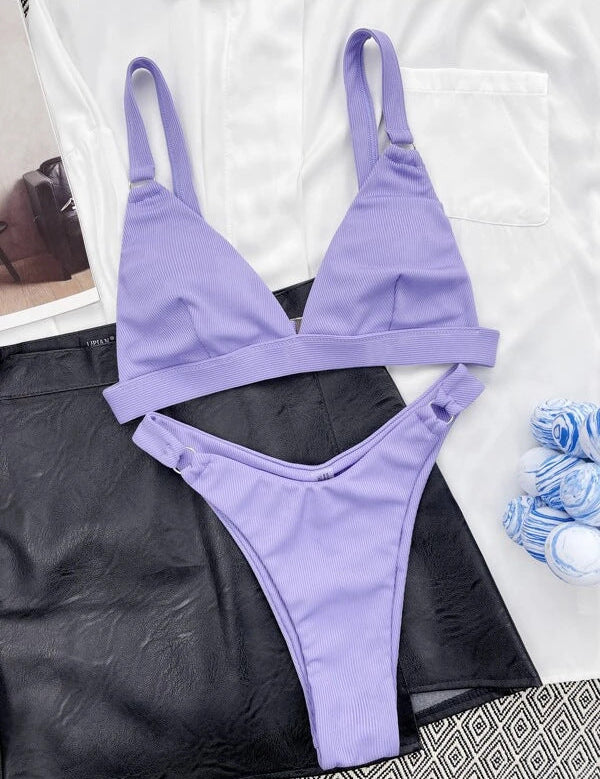 Bikini viola a due pezzi su sfondo bianco e nero, con reggiseno triangolare e slip a vita bassa. Tessuto a costine, stile estivo, moda mare.