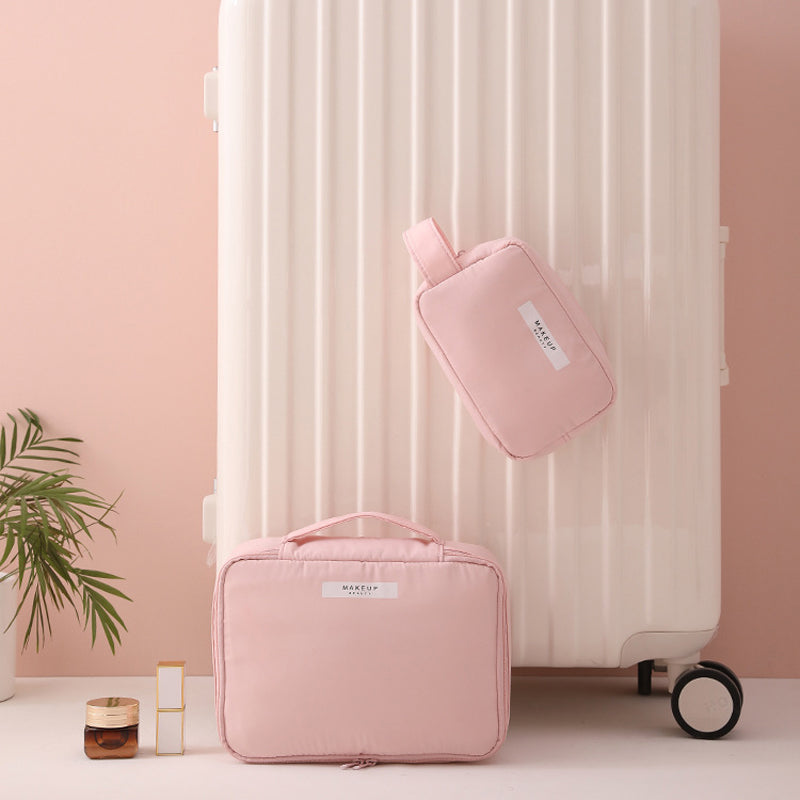 Valigia bianca con set di borse da viaggio rosa, pianta decorativa e flacone cosmetico su sfondo rosa. Accessori viaggio eleganti e funzionali.