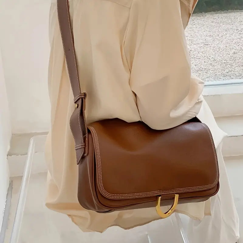 Borsa a tracolla in pelle marrone su sfondo chiaro, design elegante con fibbia dorata. Accessorio moda donna, stile casual chic.