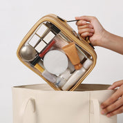 Borsa trasparente per cosmetici con cerniera, contenente trucchi e prodotti di bellezza, inserita in una borsa beige. Accessori viaggio donna.