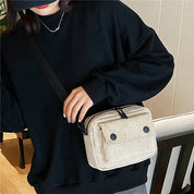 Donna con felpa nera e cappello, indossa borsa a tracolla beige con tasche frontali. Stile casual, moda urbana, accessori donna.