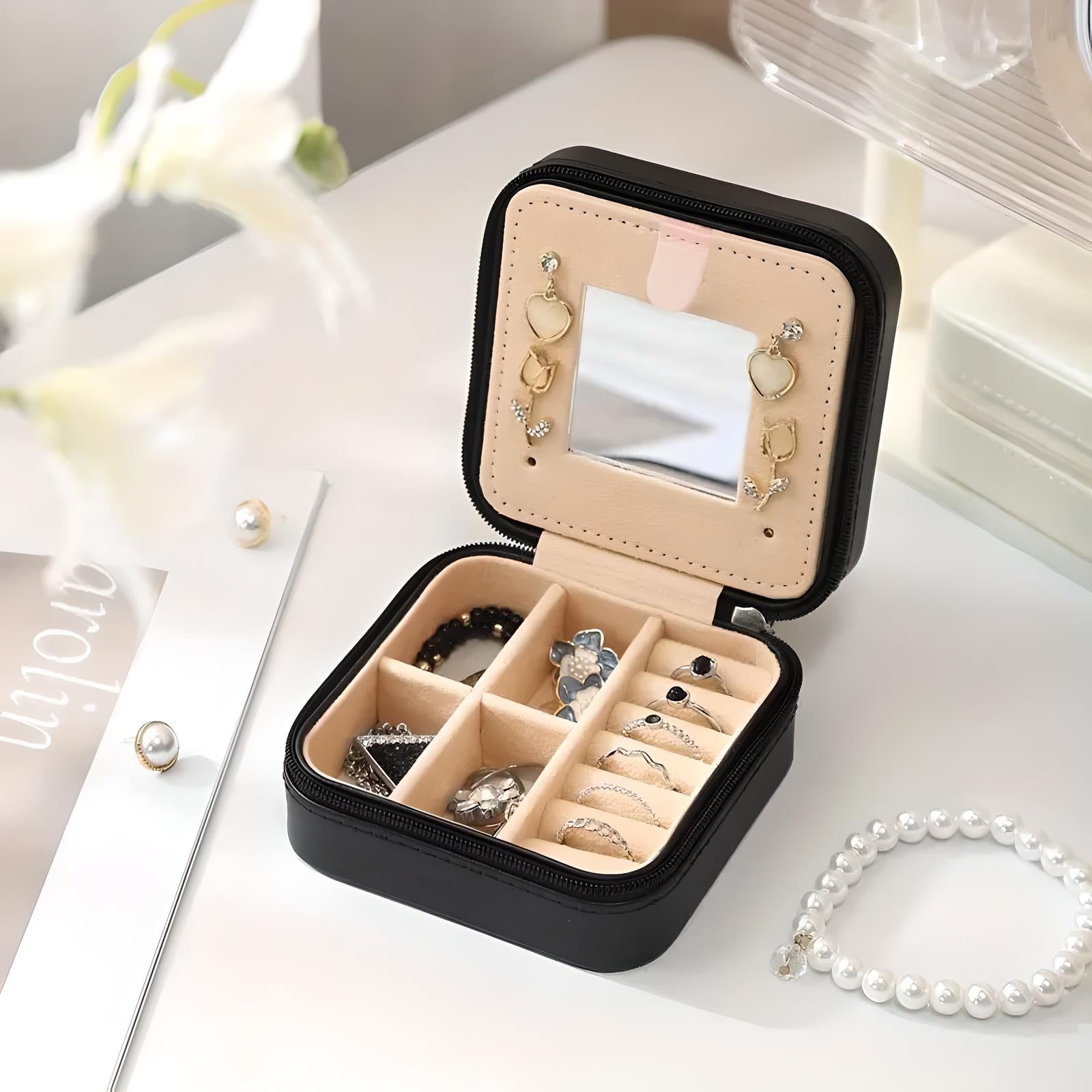 Scatola portagioie nera aperta con specchio, scomparti per anelli e orecchini, collana di perle accanto. Organizzatore gioielli elegante e compatto.