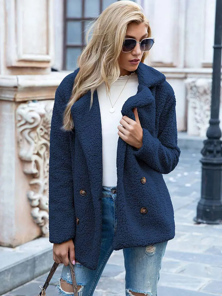 Donna con cappotto blu in pile, occhiali da sole, jeans strappati, camicia bianca. Moda autunnale casual, look urbano elegante.