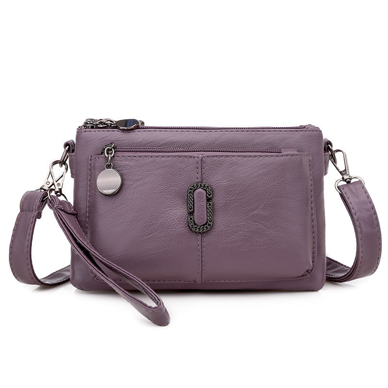Borsa a tracolla in pelle viola con cerniera, tasca frontale e decorazione metallica. Elegante accessorio moda donna, ideale per ogni occasione.