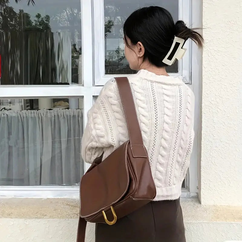 Donna di spalle con maglione a trecce bianco, fermaglio per capelli e borsa a tracolla marrone. Moda autunnale, accessori femminili eleganti.