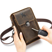 Borsa a tracolla in pelle marrone con chiusura a fibbia, logo inciso, e tasca frontale. Mani che tengono chiave auto. Accessorio moda uomo elegante.