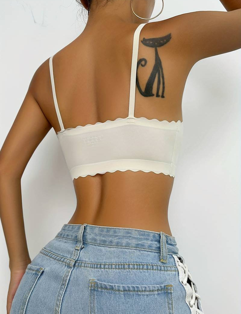 Top corto bianco con spalline sottili e bordo ondulato, indossato da una donna con jeans a vita alta. Tatuaggio di gatto nero visibile sul braccio.