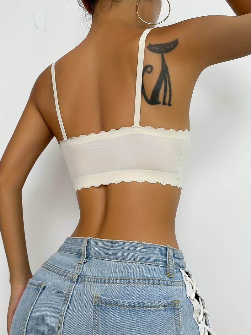 Top corto bianco con spalline sottili e bordo ondulato, indossato da una donna con jeans a vita alta. Tatuaggio di gatto nero visibile sul braccio.