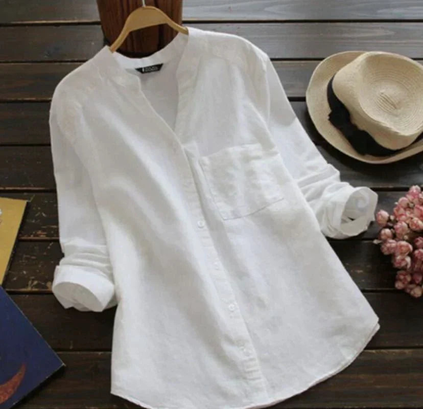 Camicia bianca in lino da donna su appendiabiti, maniche lunghe, colletto alla coreana, tasca frontale, stile casual, su tavolo di legno.
