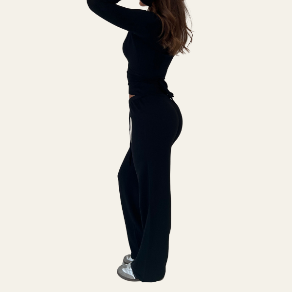 Donna in abbigliamento sportivo nero, maglia a maniche lunghe e pantaloni larghi, scarpe da ginnastica grigie. Moda casual, stile elegante.