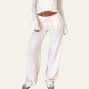 Pantaloni larghi rosa chiaro da donna, vita alta con laccio, abbinati a top bianco a maniche lunghe. Stile casual, moda femminile.
