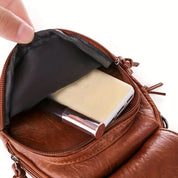 Borsa a tracolla in pelle marrone con tasca aperta, contenente smartphone e rossetto. Accessorio moda donna, elegante e pratico.