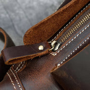 Borsa in pelle marrone con cerniera in metallo, cuciture bianche a contrasto, design artigianale, accessorio moda elegante e resistente.
