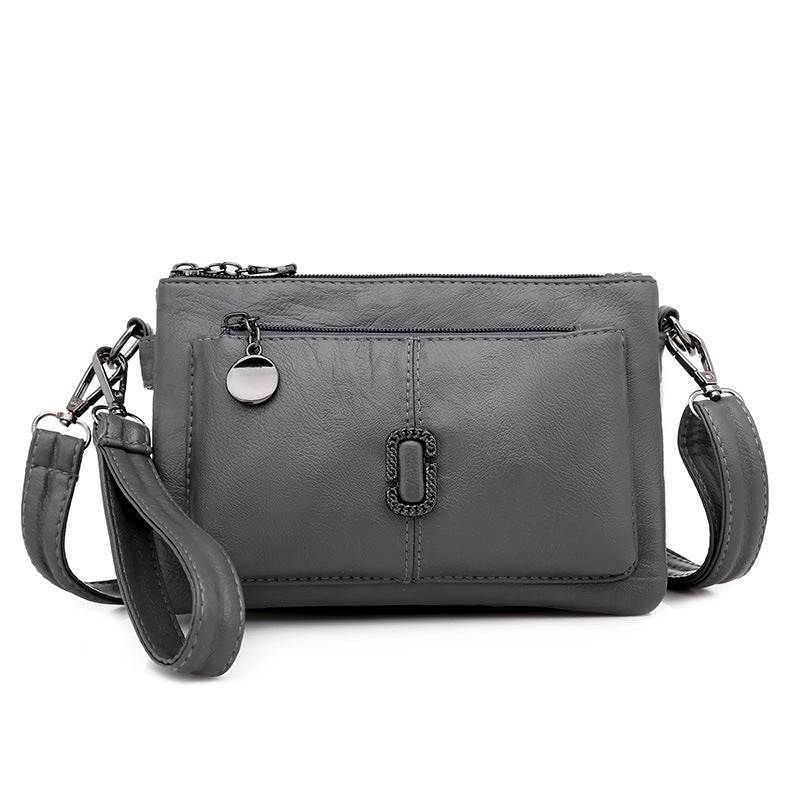 Borsa a tracolla in pelle grigia con tasca frontale, chiusura a zip e dettagli metallici. Elegante e pratica per uso quotidiano.