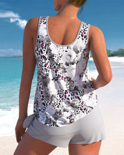 Donna in canotta floreale bianca e nera, pantaloncini grigi, su spiaggia tropicale. Moda estiva, abbigliamento casual, vacanza al mare.