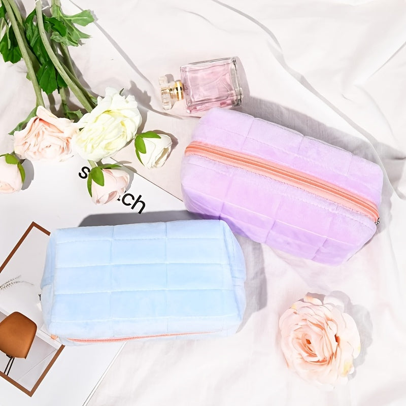 Due astucci in velluto, uno lilla e uno azzurro, con cerniera arancione, su sfondo bianco con fiori rosa e profumo. Accessori eleganti e pratici.