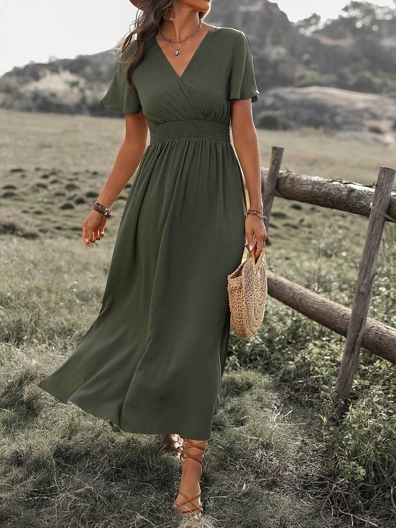 Abito lungo verde oliva estivo da donna, con scollo a V e maniche corte, indossato in un ambiente naturale. Accessoriato con borsa di paglia.