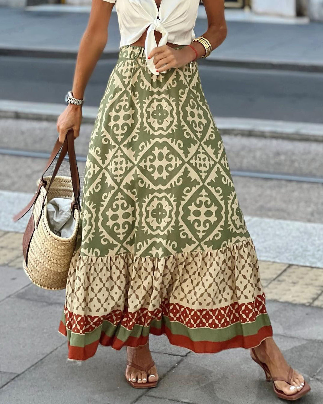 Gonna lunga boho verde con motivi geometrici, abbinata a borsa di paglia e sandali. Moda estiva donna, stile casual chic.