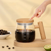 Caraffa in vetro con coperchio e manico in legno, contenente caffè. Accanto, chicchi di caffè e fetta di lime su tavolo in legno chiaro.