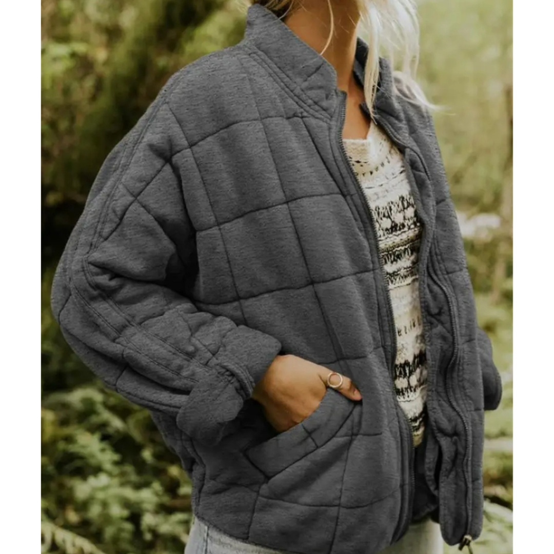Giacca trapuntata grigia da donna, stile casual, con tasche laterali, indossata su maglia bianca e nera. Perfetta per l'autunno e l'inverno.