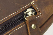 Cerniera in metallo su borsa in pelle marrone, cuciture bianche a contrasto, dettaglio artigianale, accessorio moda elegante e resistente.