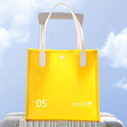 Borsa gialla da viaggio su valigia argentata, cielo azzurro sullo sfondo. Accessori viaggio, borsa tote impermeabile, design moderno.