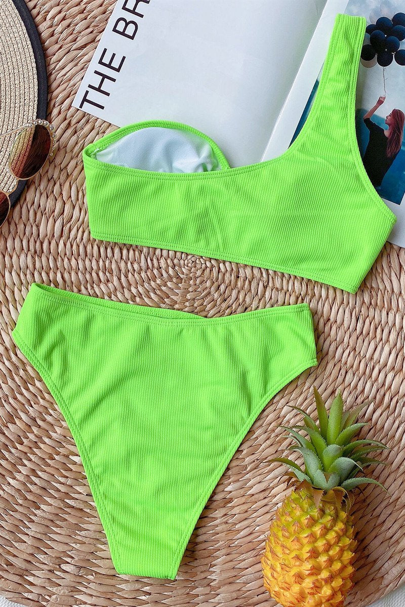 Costume da bagno donna verde neon, due pezzi, su tappeto di paglia con ananas e cappello. Moda estiva, beachwear, tendenze 2023.