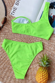 Costume da bagno donna verde neon, due pezzi, su tappeto di paglia con ananas e cappello. Moda estiva, beachwear, tendenze 2023.