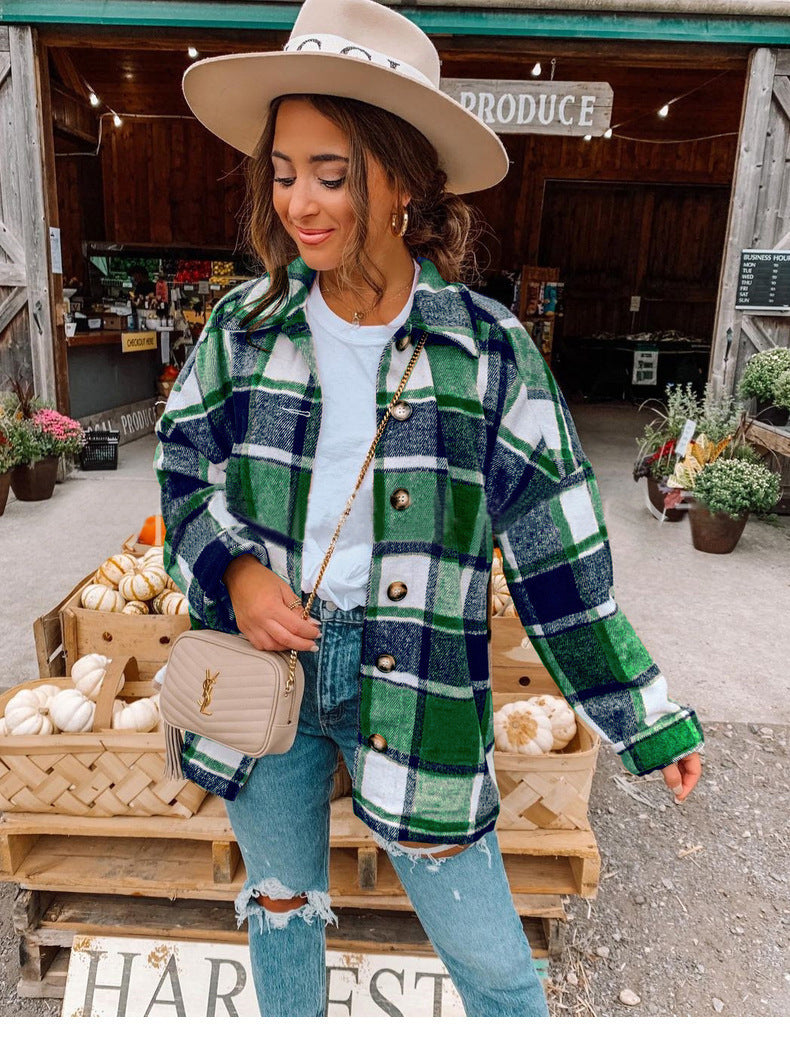 Donna con cappello beige e camicia a quadri verde e blu, davanti a un mercato agricolo. Indossa jeans strappati e borsa a tracolla.