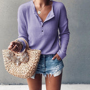Donna con maglia viola a maniche lunghe, shorts di jeans e borsa di paglia intrecciata. Moda casual estiva, abbigliamento femminile trendy.