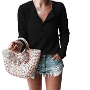 Maglia nera a maniche lunghe con bottoni, abbinata a shorts di jeans strappati e borsa intrecciata beige. Look casual estivo donna.