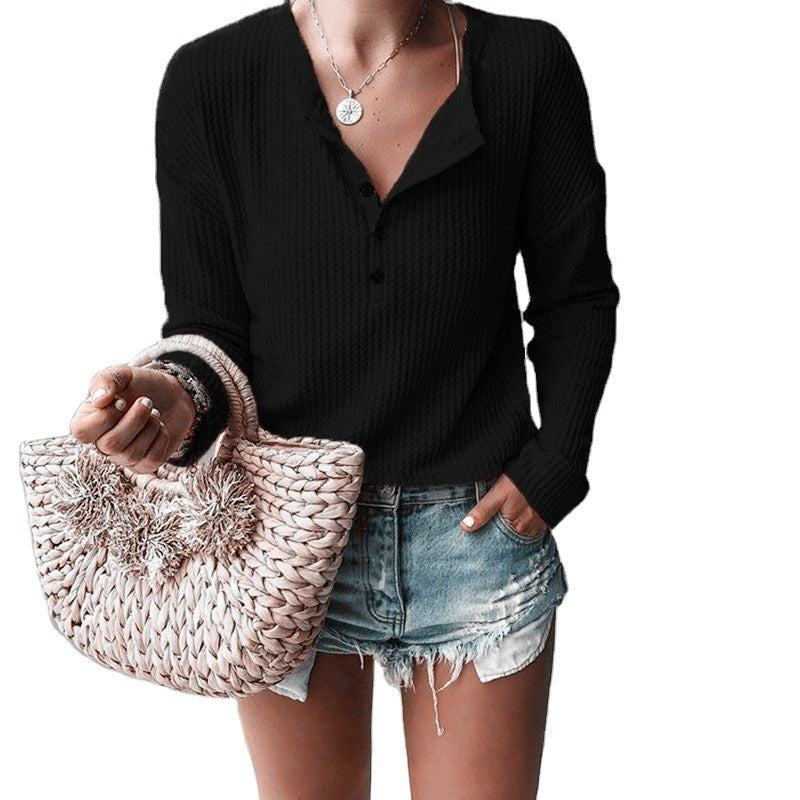 Maglia nera a maniche lunghe con bottoni, abbinata a shorts di jeans strappati e borsa intrecciata beige. Look casual estivo donna.