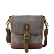 Borsa a tracolla in tela grigia e marrone con fibbia in metallo, tasca frontale e tracolla regolabile. Accessorio moda unisex, stile casual.