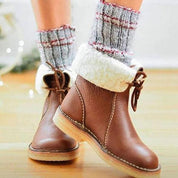 Stivali invernali marroni con fodera in pelliccia sintetica, indossati con calzini grigi a righe rosse. Scarpe calde e comode per l'inverno.